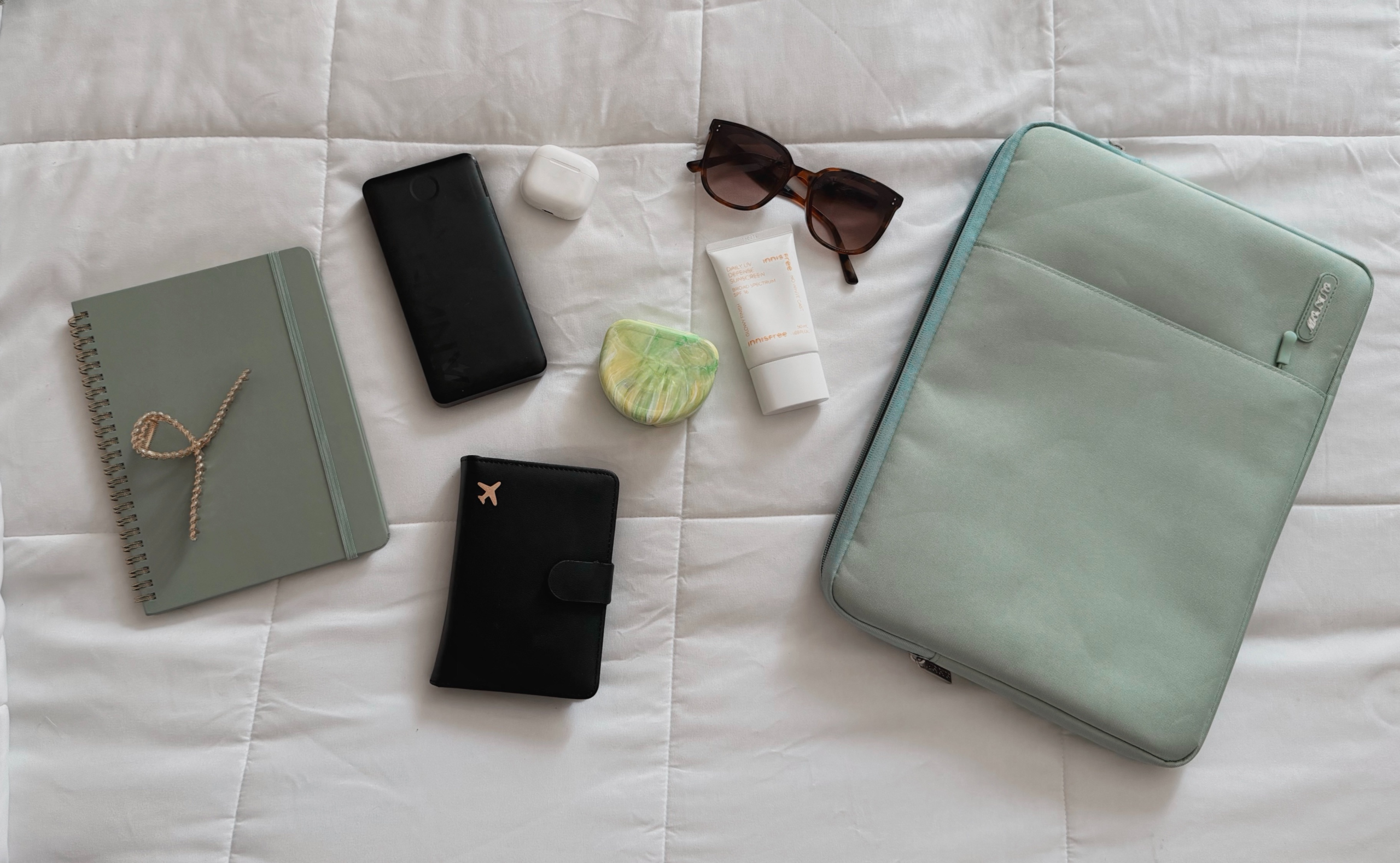 Flat lay of carry-on travel essentials including passport, toiletries, electronics, snacks, water bottle, and personal items for a flight